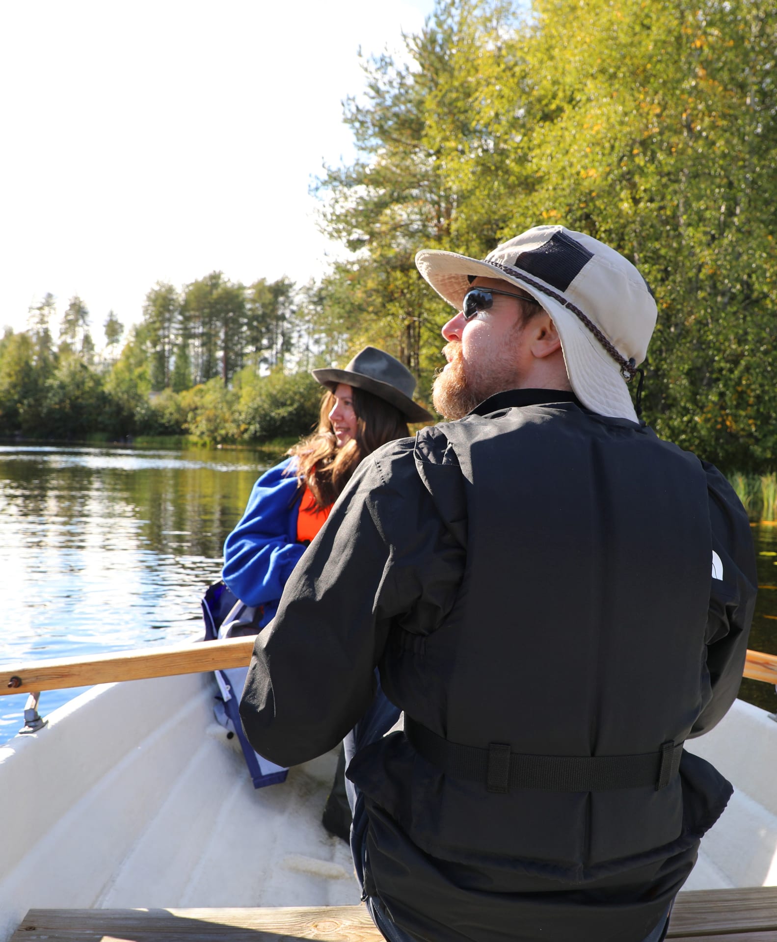 A young couple rowing leisurely across the completely still Lake Korpijärvi on a sunny day.