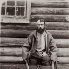 Old black and white picture of a criminal with half shaved head in front of a wooden building