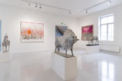 Tauluja ja härkäveistos valoisassa näyttelytilassa. Paintings and a bull sculpture in a bright exhibition space.