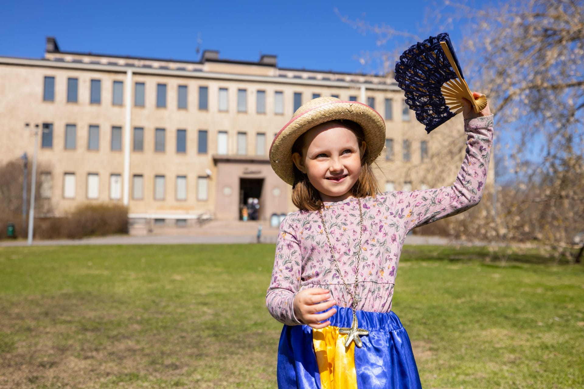A smiling girl dressed in an old-fashioned role costume. In the background is the Museum of Northern Ostrobothnia.