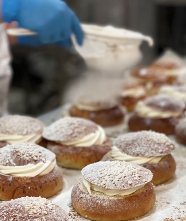 The baker dusts the buns with powdered sugar.