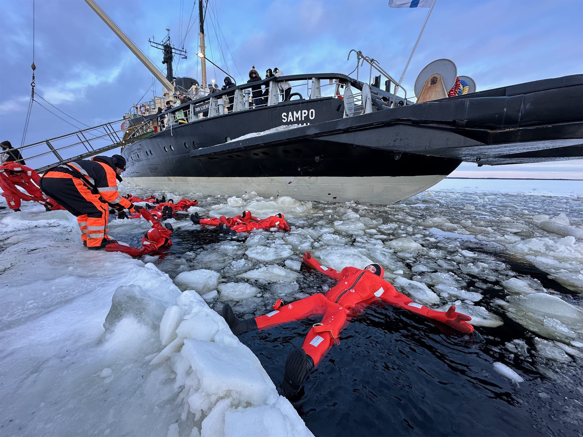 people floating in ice sea water in survival suits next to the icebreaker sampo