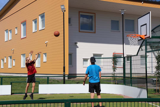 Kaksi poikaa pelaa koripalloa monitoimiareenalla.