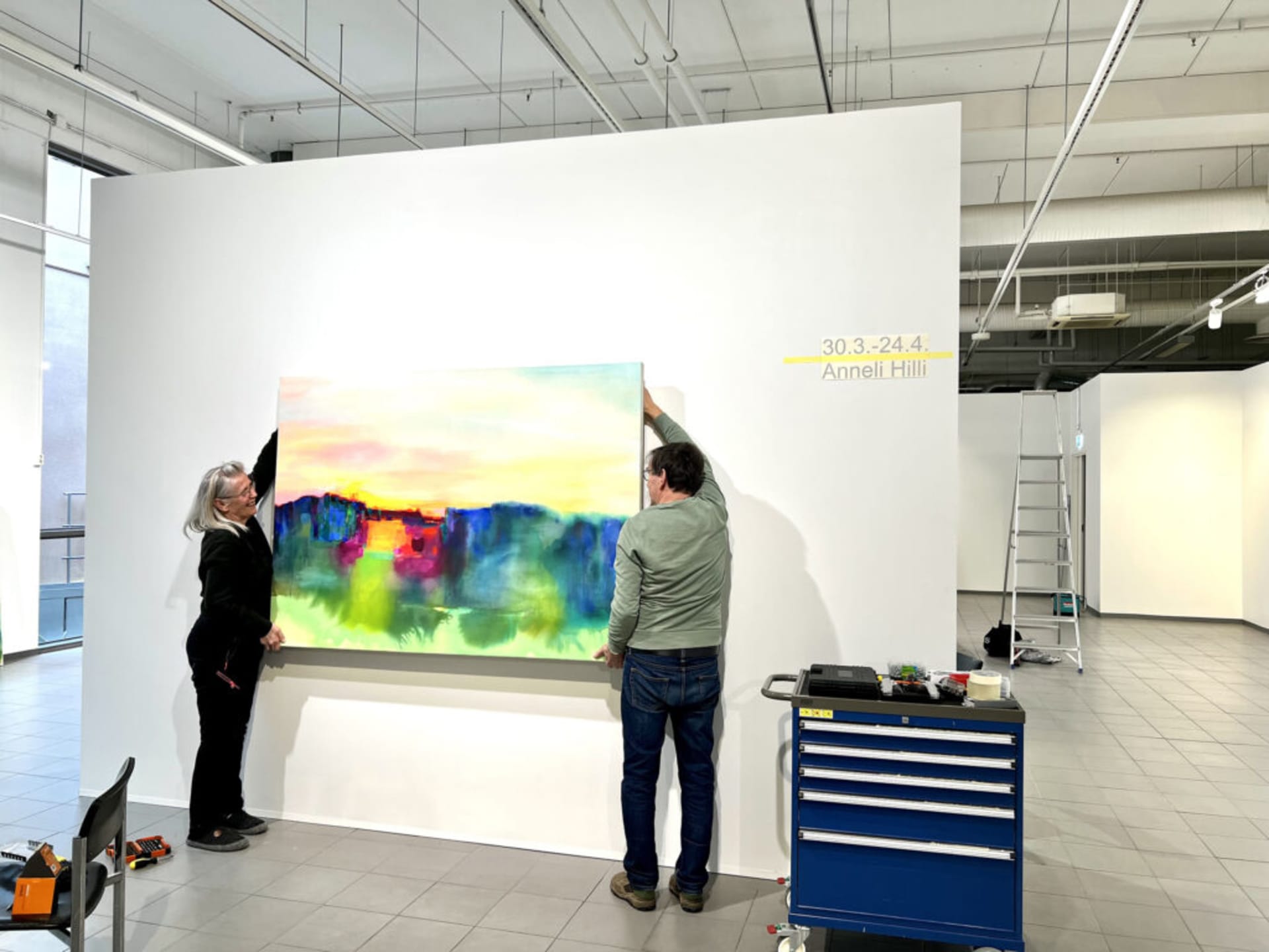 New art exhibitions every four weeks, artist Anneli Hilli lifting her painting on the wall.