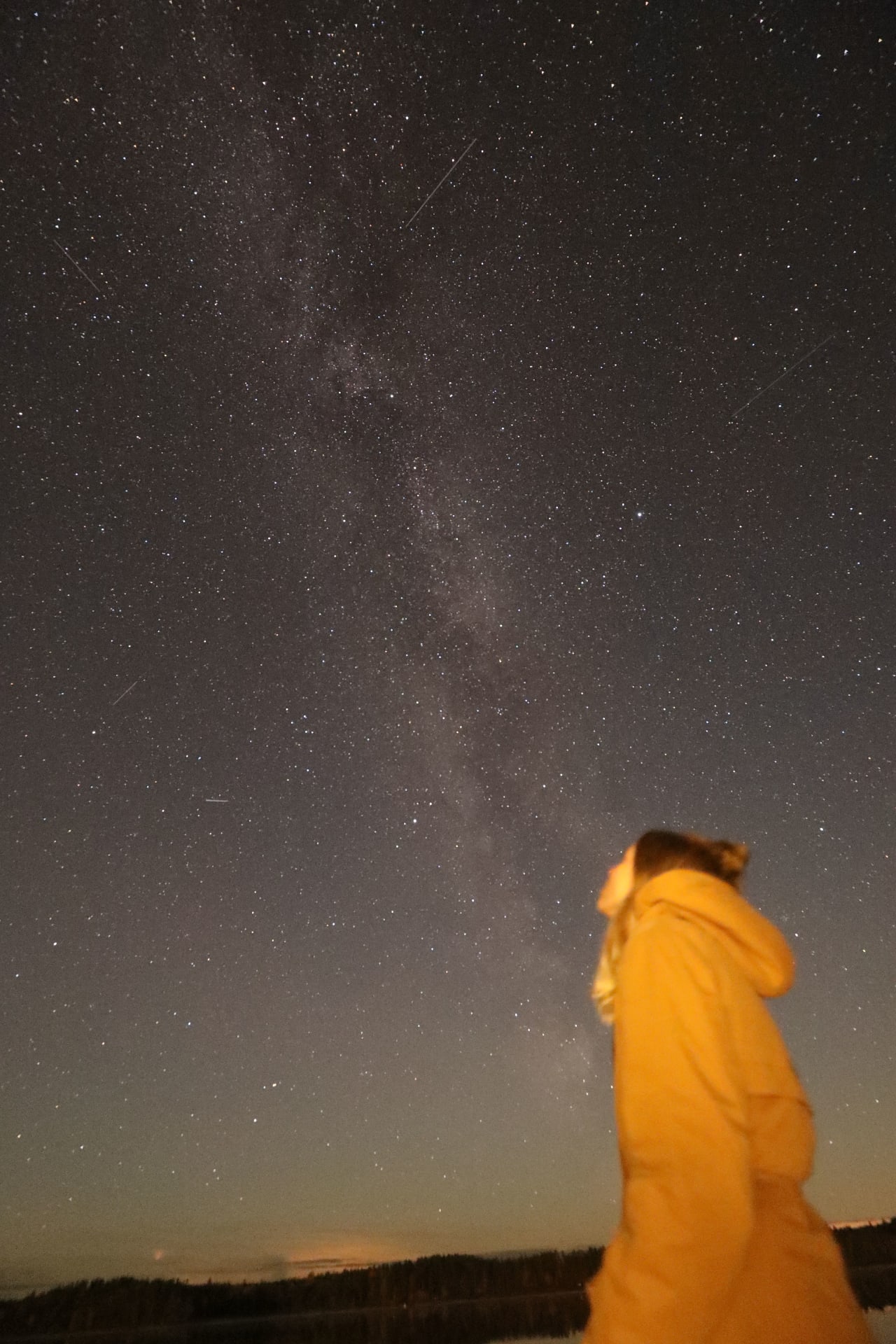 A woman stands outdoors in the silent darkness, marveling at the Milky Way with thousands of stars overhead.