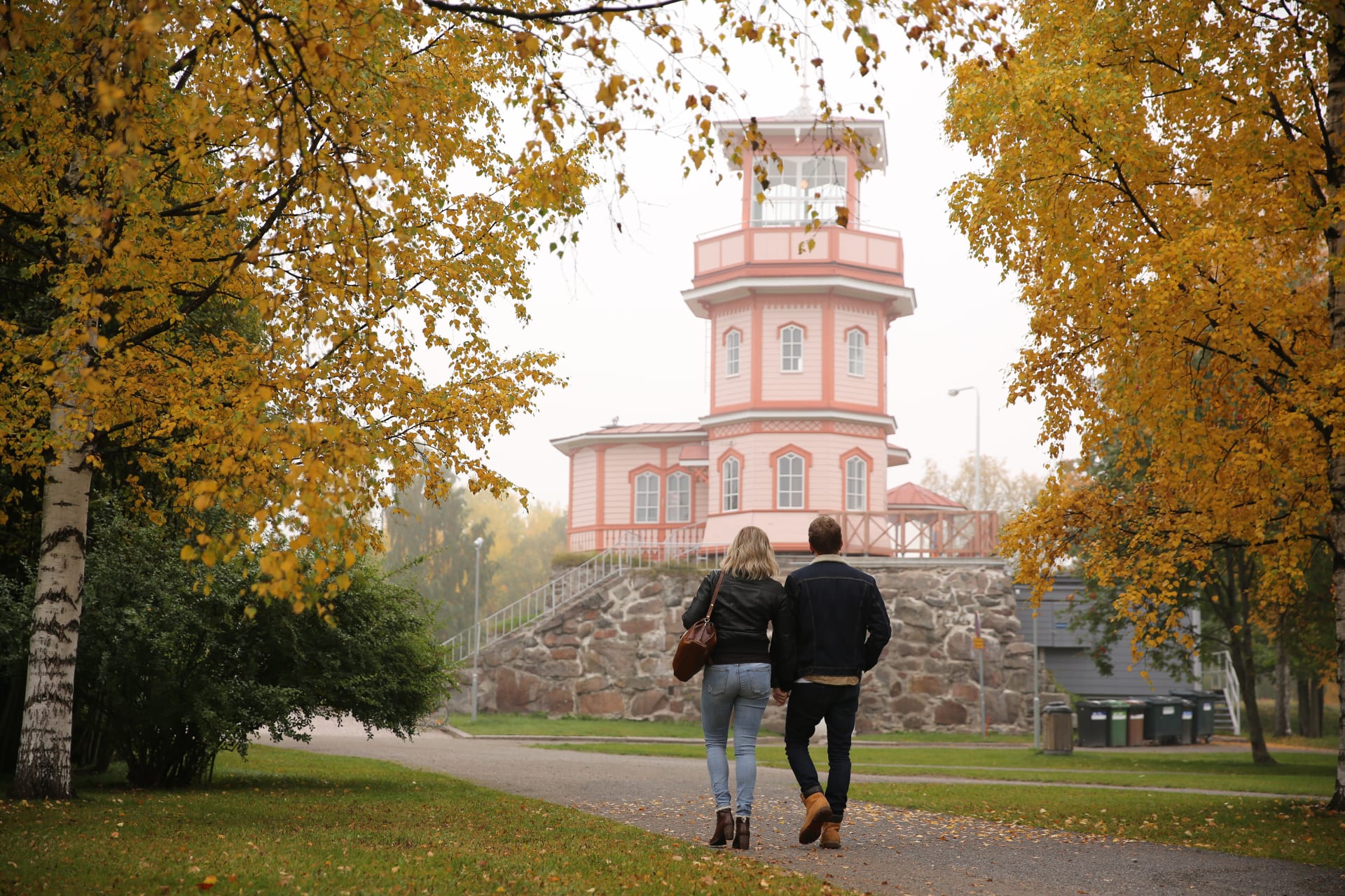 Woman and man walking towards Tähtitorni tower in autumn.