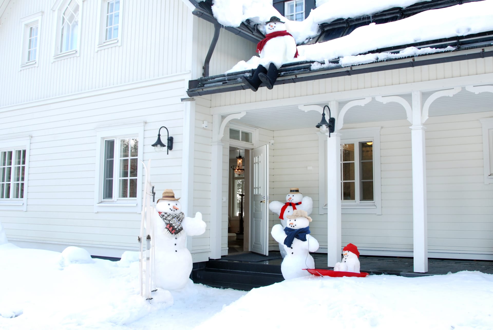 A snowman family welcomes guests at the entrance of Villa Cone Beach, including parents, a child, a toddler in a sled, and a daring kid sitting on the roof with boots hanging over the edge.