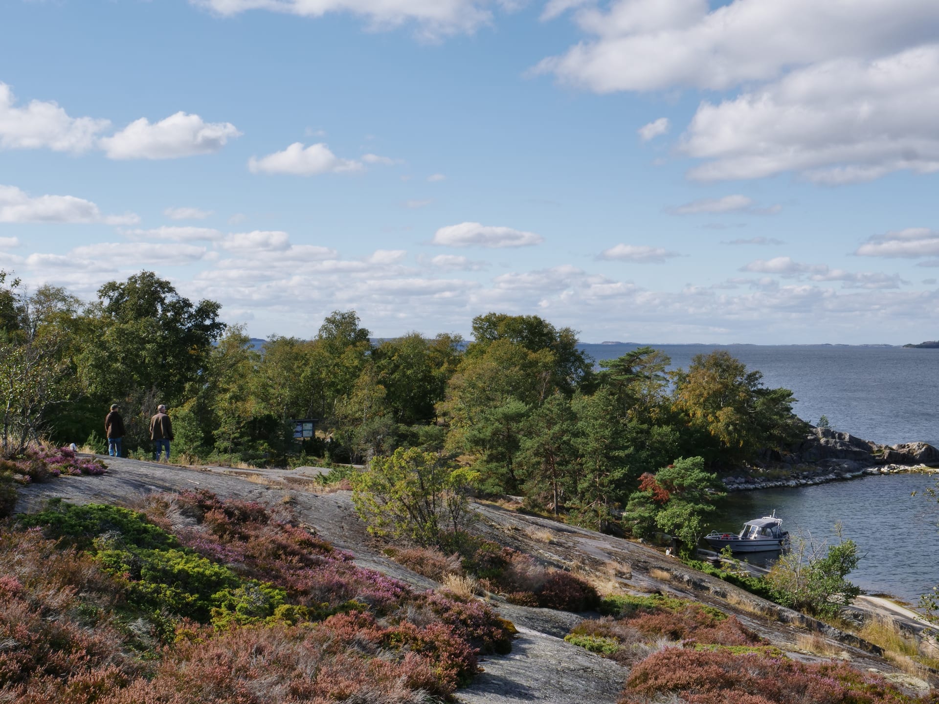 Kallio kaartuu jyrkästi alas oikealle, kohti merta. Kuvan vasemmassa laidassa kävelee kaksi ihmistä. Rannassa on vene. The cliff curves sharply down to the right, towards the sea.  There is a boat on the beach Kallio kaartuu jyrkästi alas oikealle, kohti merta. Kuvan vasemmassa laidassa kävelee kaksi ihmistä. Rannassa on vene. The cliff curves sharply down to the right, towards the sea.  There is a boat on the beach