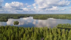 Maisema virkistysalueelta järvelle päin, maisemassa havumetsää, järvi, saaria ja vene.