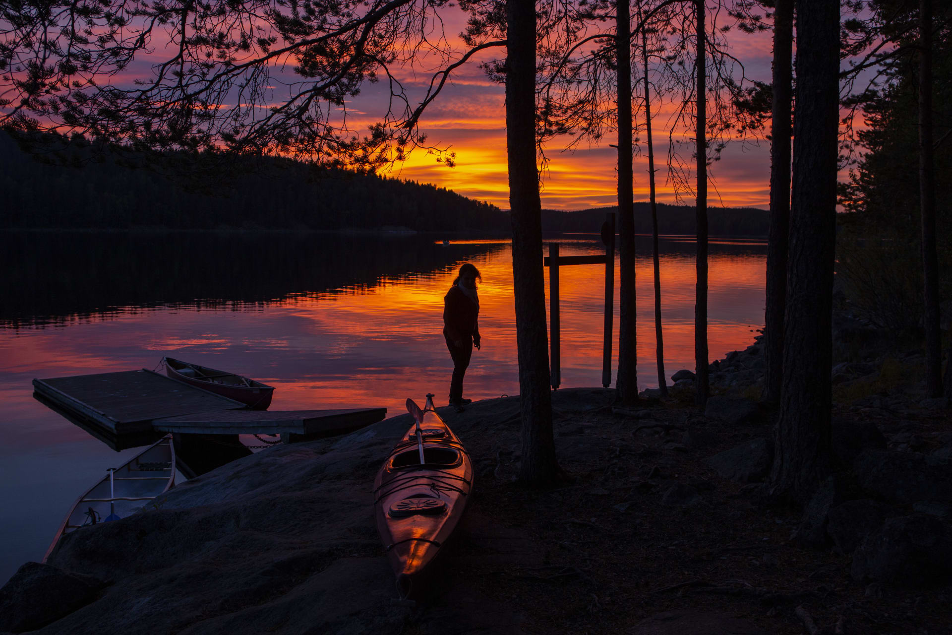 Kesäinen auringonlasku järvellä. Rannassa retkeilijä ja kajakki, taustalla järvimaisema. Kuva: Saara Lavi