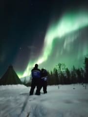 Two people gazing at the night sky with Aurora Borealis.