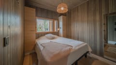 Cozy bedroom with wooden walls. Double bed and a blanket on top of it.