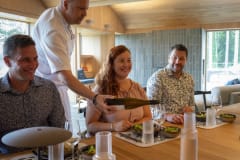 Keittiömestari kaataa viiniä asiakkaalle Serlachius Taidesaunan ruokapöydän ääressä.