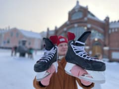 A person holding hockey skates outside of the Oulu Market Hall