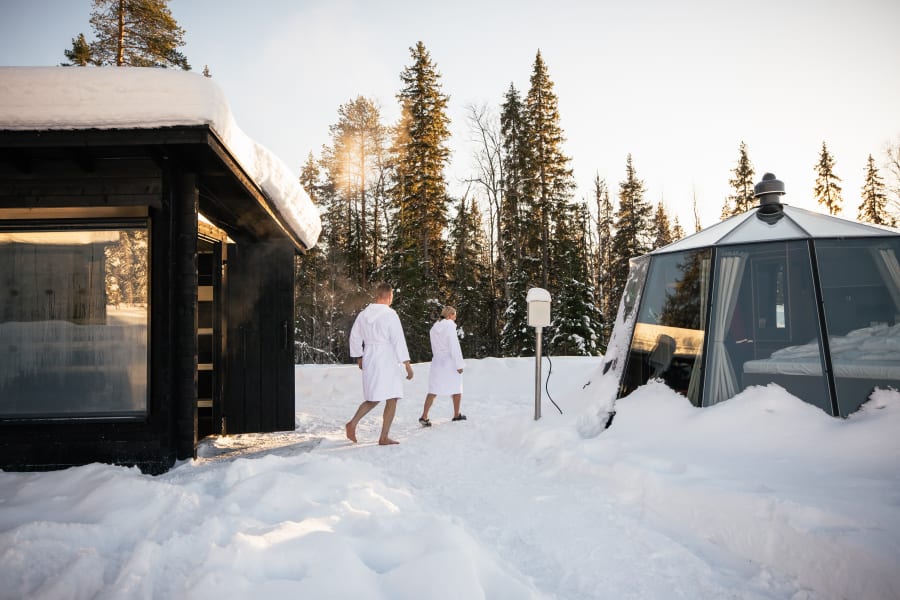 A couple walks from their private sauna to their Aurora Hut