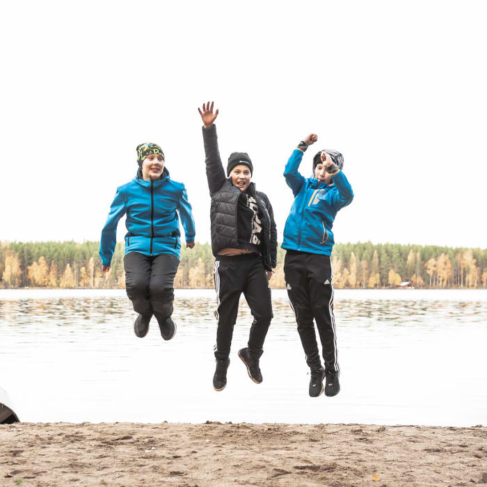 Three happy boys jumping up in the air by the lake in the autumn time.