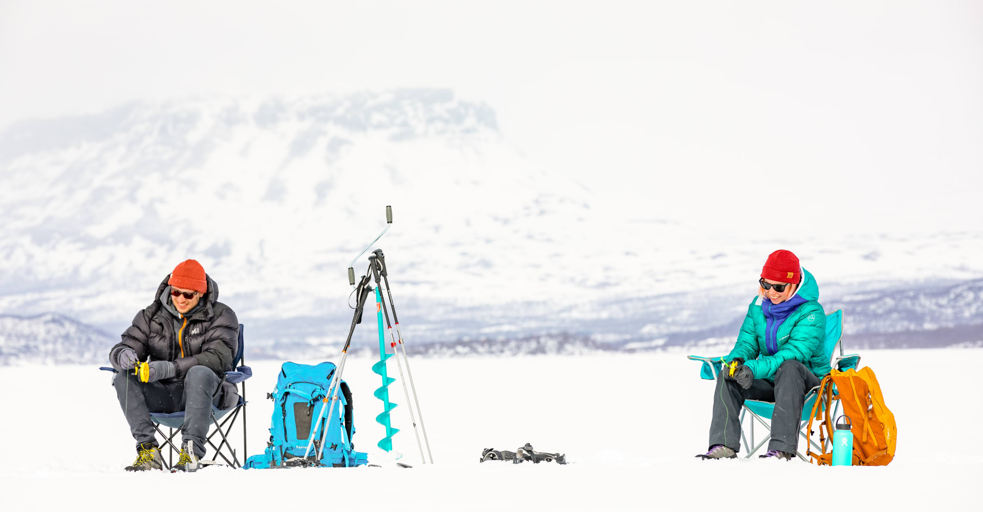 Kaksi retkeilijää pilkillä Kilpisjärven jäällä. Taustalla luminen Saanatunturi. Kuva: Rami Valonen
