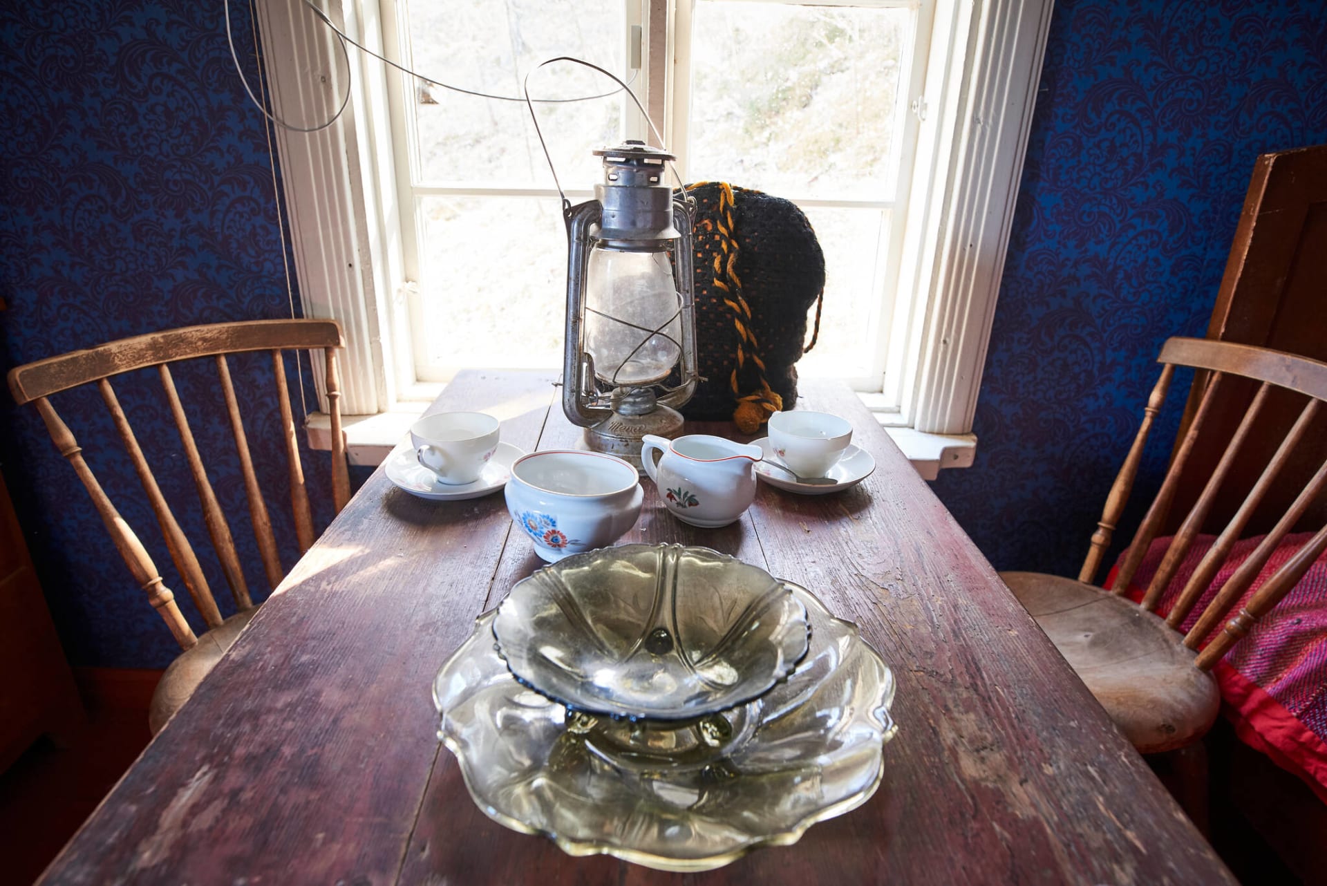 Puinen pöytä ikkunan edessä katettuna öljylampulla ja kahvikupeilla