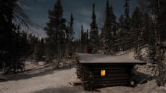 Kuusikon keskellä pieni tupa ensilumen aikaan. Tuvan ikkunasta loistaa valo. A small hut is in the middle of the forrest. There have been the first snow. There is a little light through the window.Photo: Konsta Verta