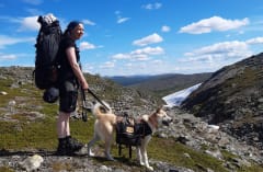 Retkeilijä ihailee kurua, jossa on vielä vähän lunta. Retkeilijän mukana oleva koira on kytketty hihnaan. Hiker with big backpack is watching the valley, where is lot of rocks. There is a bit snow. The dog is on a leash. Photo: Veera Ruokonen