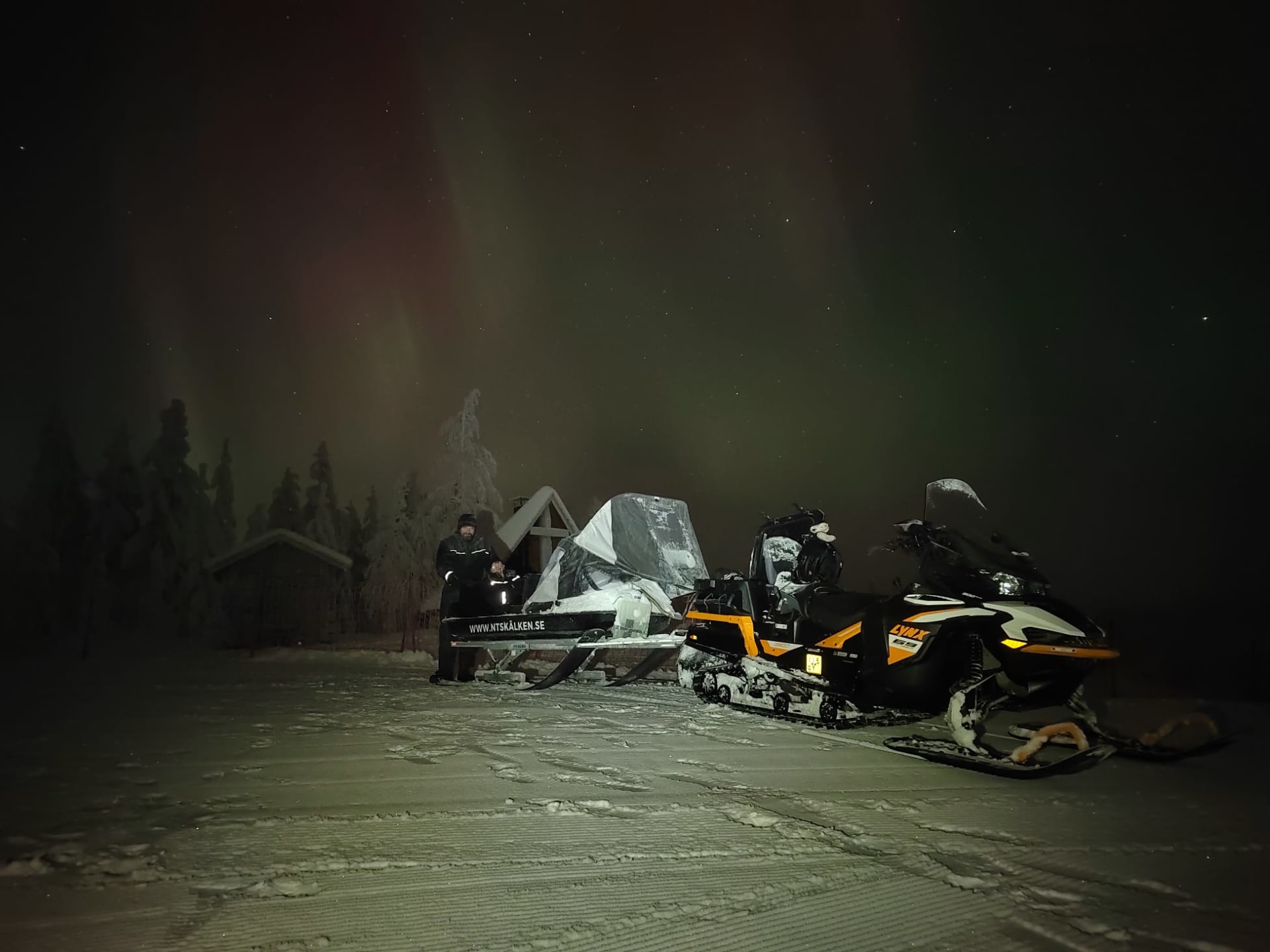 Snowmobiles in stand still in front of Aurora Borealis