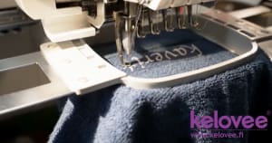 Embroidery machine stitching on navy blue towel. Brodeerauskone brodeeraa tummansinistä pyyhettä.