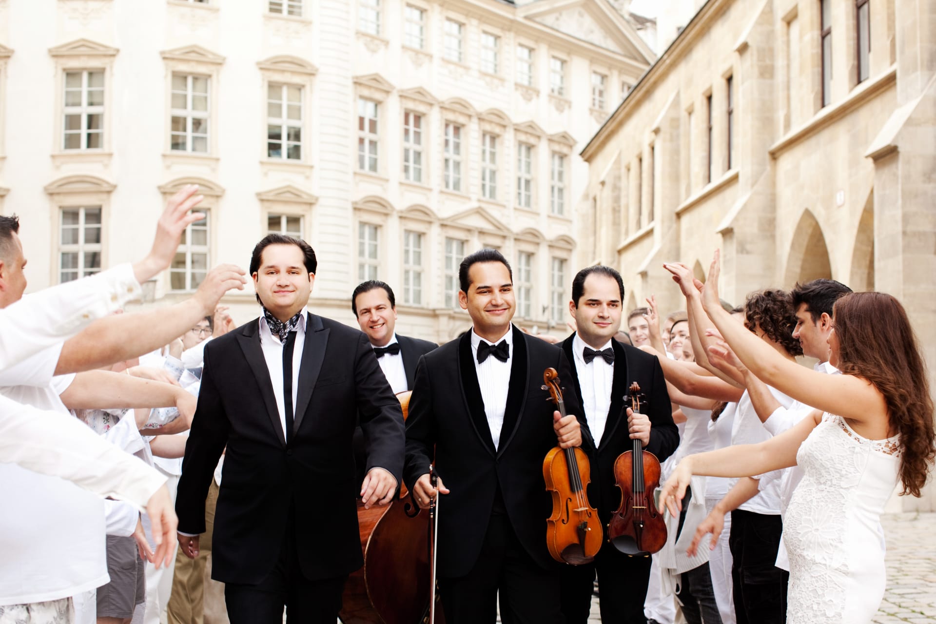 Musicians of the Janoska Ensemble walking down the street smiling, with people cheering for them on both sides